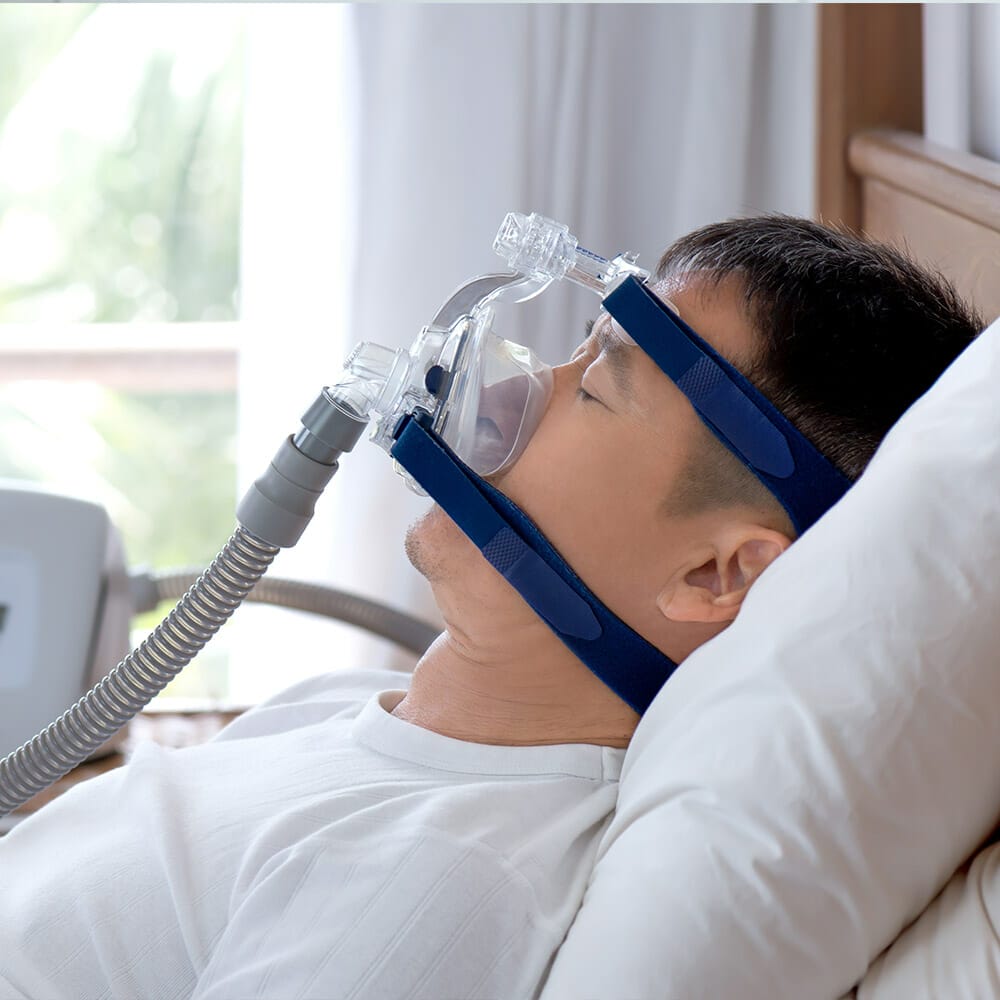 A man lies in bed wearing a CPAP mask to treat sleep apnea