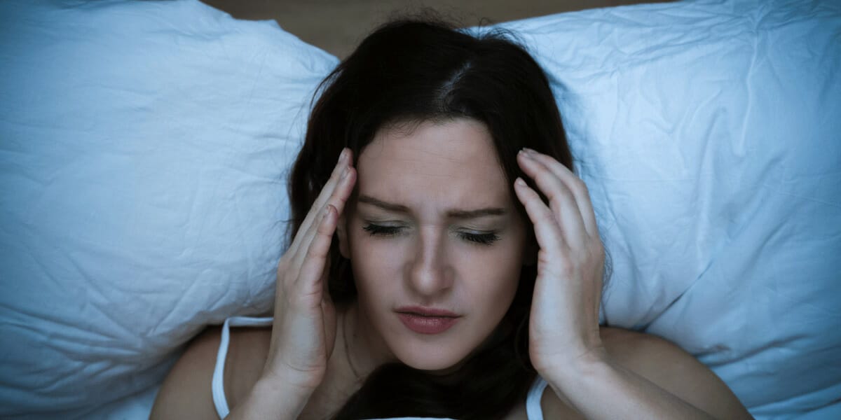 woman laying in bed touching her had, looks in pain