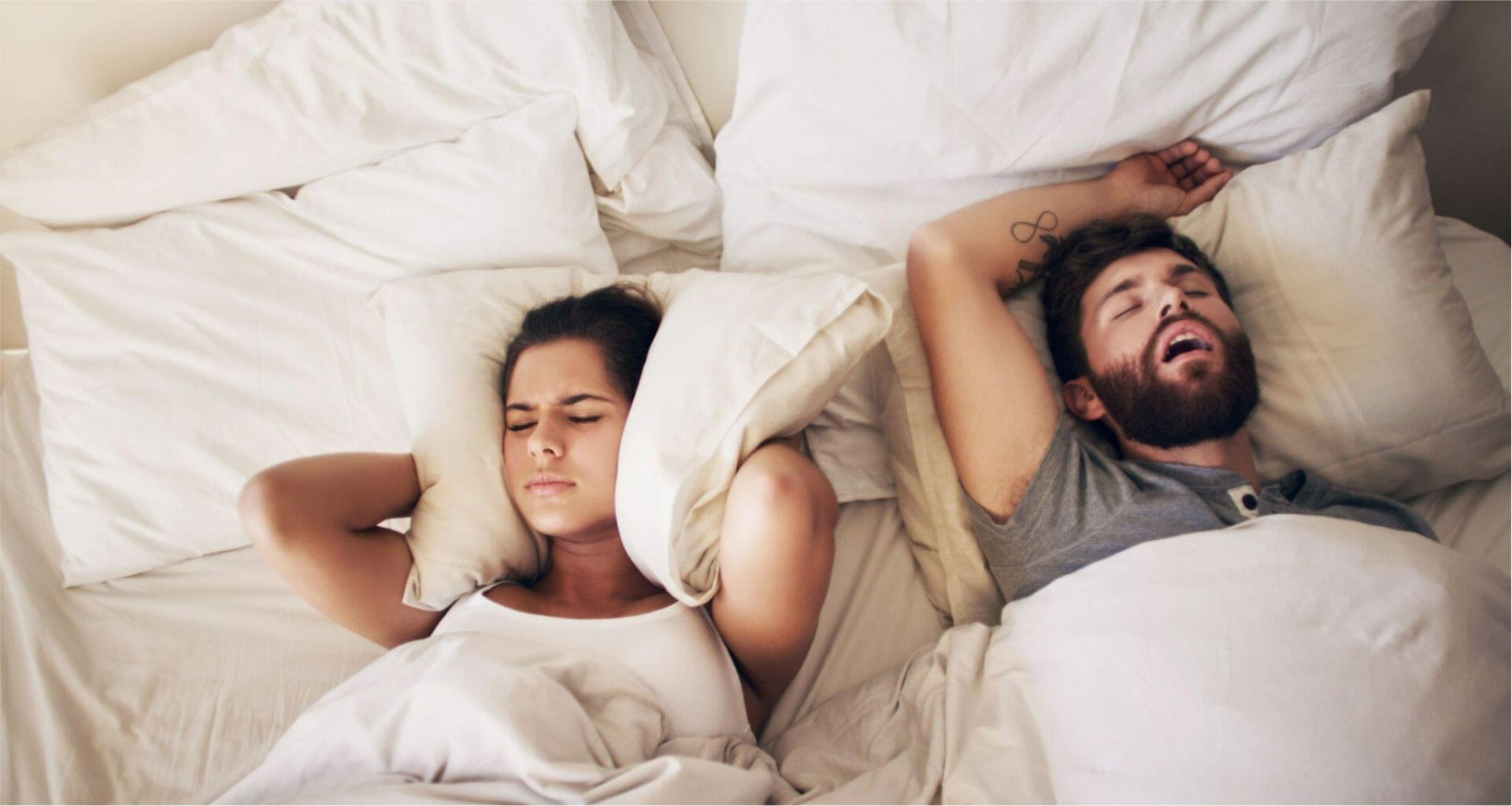 man snoring, his partner holding pillows to her ears