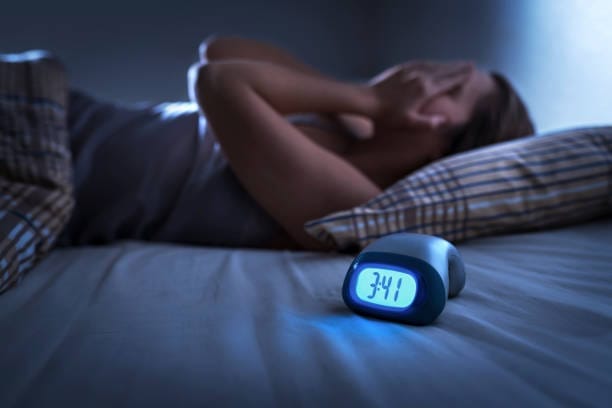 Woman lying awake in bed at 3:41 a.m., covering her face in frustration next to a digital clock
