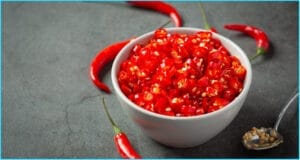 Bowl of chopped red chili peppers surrounded by whole chilies