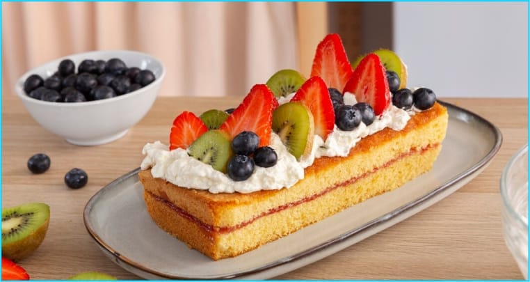 Decorative cake topped with whipped cream, strawberries, kiwi, and blueberries 