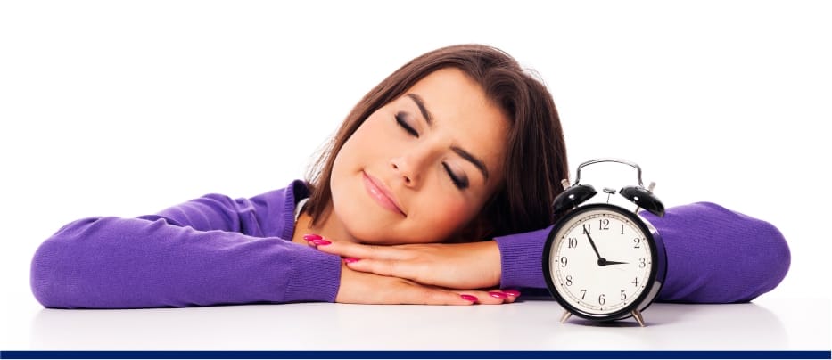 Smiling woman resting her head on folded arms beside a clock, symbolizing good sleep or nap time