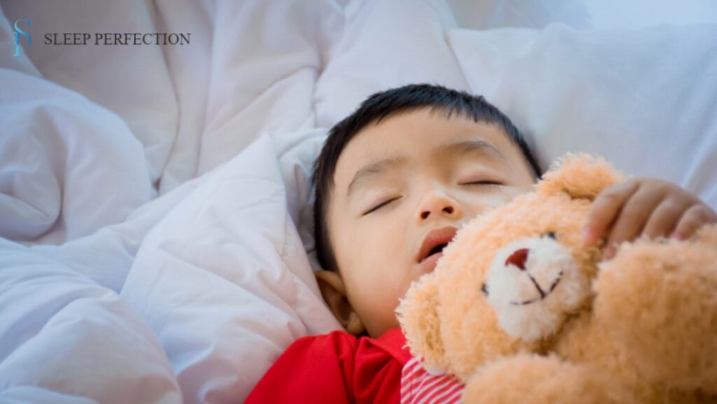 Young child sleeping while cuddling a teddy bear under a white blanket
