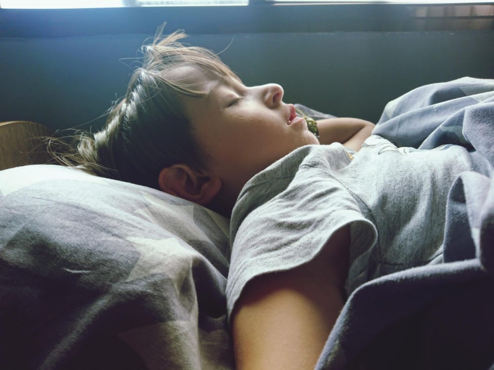 A little boy sleeping peacefully on a bed during daytime