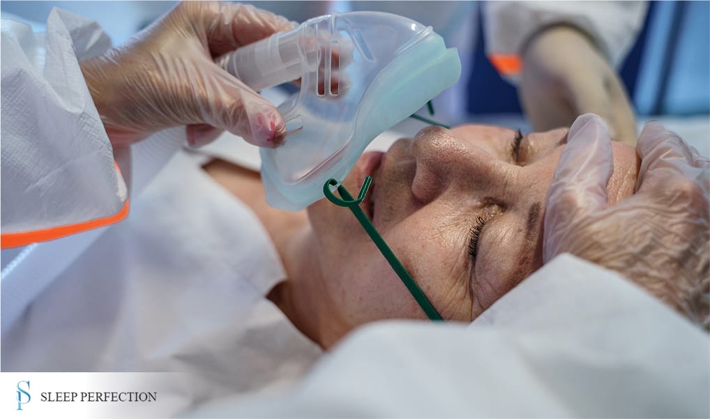 A medical professional places an oxygen mask on a patient lying down, likely preparing for treatment 