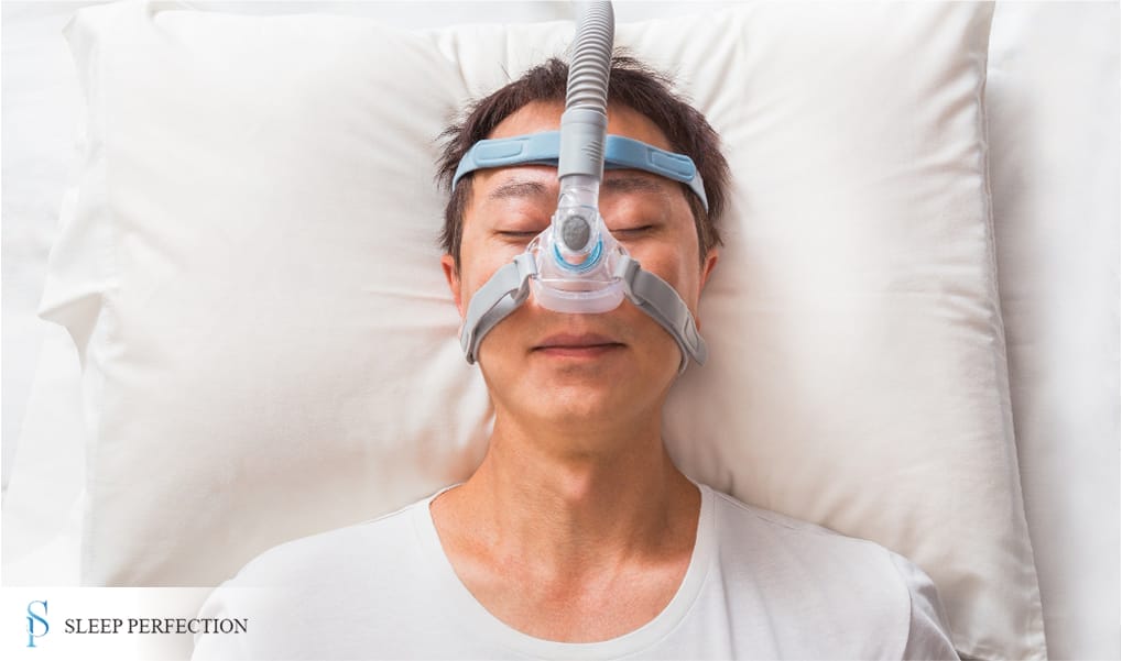 A man lies on his back wearing a CPAP mask for sleep apnea therapy while resting peacefully