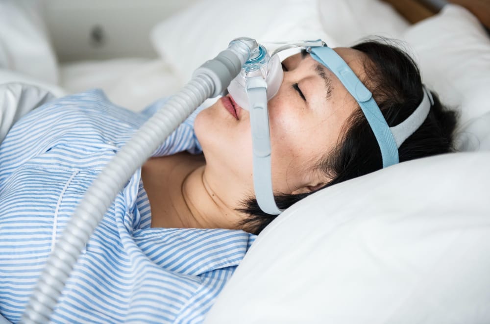 A woman lies in bed asleep while wearing a CPAP mask to treat sleep apnea