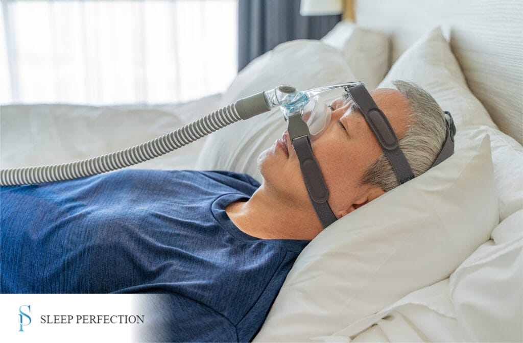 An older man lies in bed peacefully while using a CPAP machine for sleep apnea treatment