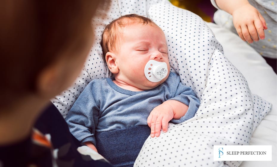 A baby sleeps soundly with a pacifier in its mouth, nestled in a polka-dot cushion